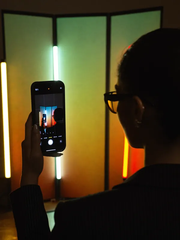 A woman in a dark studio filming on her phone between tall light panels